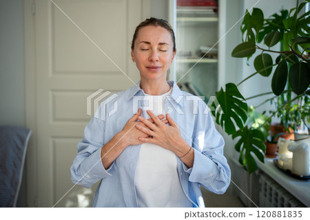 Peaceful woman standing with closed eyes, folding one's arms on chest doing breathing exercises. 120881835