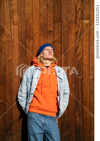 Relaxed skinny long-haired male with eyes closed leaning on wooden wall outdoors in bright sunny day Relaxed skinny long-haired male with eyes closed leaning on wooden wall outdoors in bright sunny day 120881851