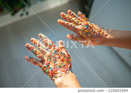 Sticky sweet multicolored baking decorations on women's hands in rays of sunlight, festive mood. Sticky sweet multicolored baking decorations on women's hands in rays of sunlight, festive mood. 120881894