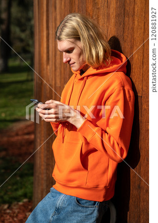 Good-looking sexy confident long-haired hipster boy leaning on wall outdoors in bright sunny day Good-looking sexy confident long-haired hipster boy leaning on wall outdoors in bright sunny day 120881927
