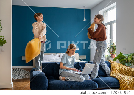 Mother working on laptop while her active noisy children playing with pillows and having fun Mother working on laptop while her active noisy children playing with pillows and having fun 120881995