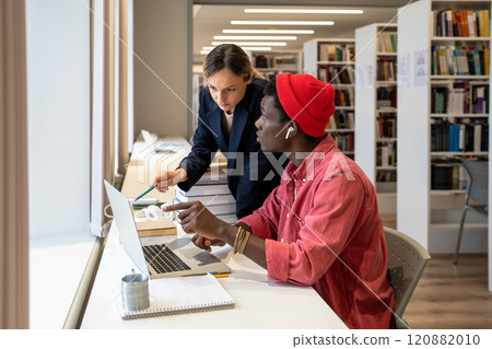Focused multiracial students couple speak about study project exam with laptop in university library 120882010