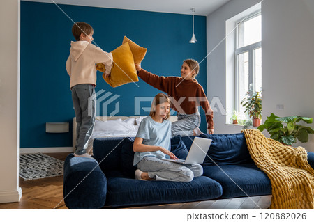 Playful european siblings boy and girl pillow fighting distracting busy mom relaxing on sofa at home Playful european siblings boy and girl pillow fighting distracting busy mom relaxing on sofa at home 120882026