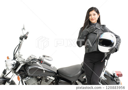 A biker girl standing next to a bike, holding a helmet and introducing the bike 120883956