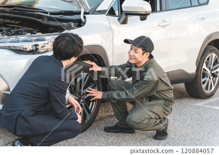 A businessman in a suit and a male auto mechanic in overalls having a conversation in front of a car A businessman in a suit and a male auto mechanic in overalls having a conversation in front of a car 120884057