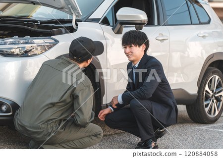 一位穿著西裝的商人和一位穿著連身褲的男性汽車修理工正在車前交談。 120884058