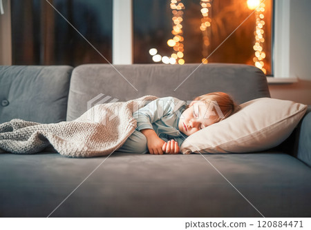 Cozy evening: child sleeping on sofa with warm blanket in illuminated room Cozy evening: child sleeping on sofa with warm blanket in illuminated room 120884471