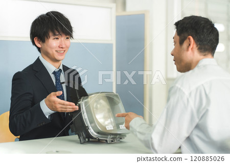 A male service front desk attendant and a male customer at the reception desk of an auto repair shop A male service front desk attendant and a male customer at the reception desk of an auto repair shop 120885026