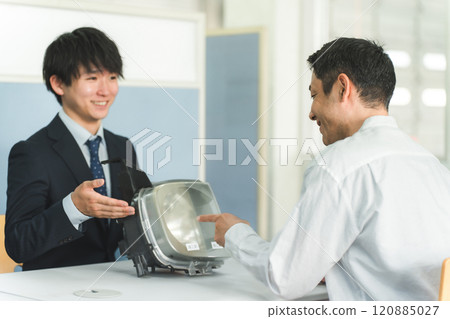 A male service front desk attendant and a male customer at the reception desk of an auto repair shop A male service front desk attendant and a male customer at the reception desk of an auto repair shop 120885027
