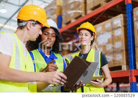 A diverse team of warehouse personnel is conducting a comprehensive stock inventory using laptop computers within the confines of the warehouse. 120885529