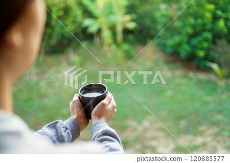 Unrecognizable Asian woman enjoy drinking a coffee at the corridor with the rural environment background and beautiful sunlight in the morning. Delighted Asian woman drinking a hot coffee in morning. Unrecognizable Asian woman enjoy drinking a coffee at the corridor with the rural environment background and beautiful sunlight in the morning. Delighted Asian woman drinking a hot coffee in morning. 120885577