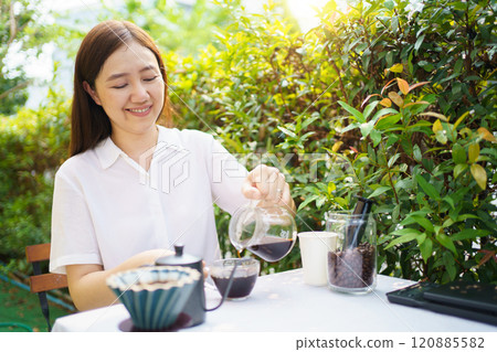Happy Asian beautiful woman making a specialty coffee in morning at her backyard garden, woman brewing a coffee by dripping or pouring over a hot water. 120885582