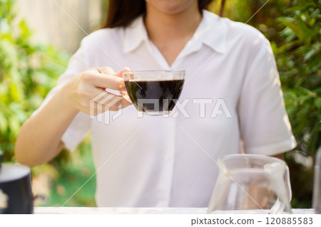 Happy Asian beautiful woman brewed a drip coffee in her backyard in morning. Delighted woman enjoy drinking a cup of black coffee on the outdoor dinning table. Happy Asian beautiful woman brewed a drip coffee in her backyard in morning. Delighted woman enjoy drinking a cup of black coffee on the outdoor dinning table. 120885583