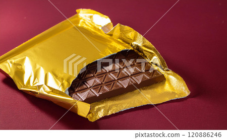 A chocolate bar is sitting in a gold wrapper 120886246