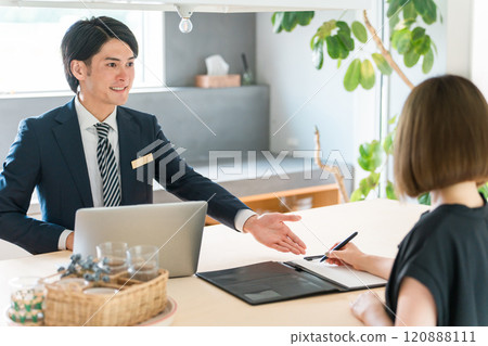 A male salesman in a suit asking for a signature on a contract/agreement form and a female customer signing it 120888111