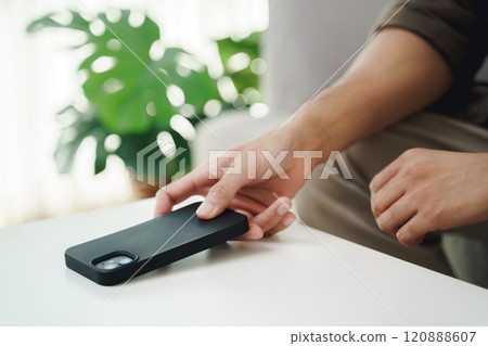 Close up of a man's hand is to put his mobile phone on the table after stopping using it. 120888607