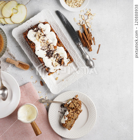 A piece of Spicy apple, nuts and oats loaf cake decorated with cream on a white plate, gluten free, top view, copy space 120888938
