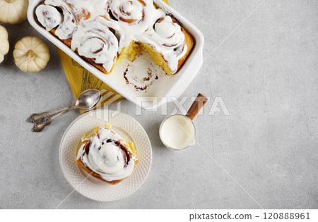 Fragrant freshly baked Cinnamon rolls or cinnabons with pumpkin covered with white cream glaze on the plates on white background. Cinnabons recipe. top view, copy space Fragrant freshly baked Cinnamon rolls or cinnabons with pumpkin covered with white cream glaze on the plates on white background. Cinnabons recipe. top view, copy space 120888961