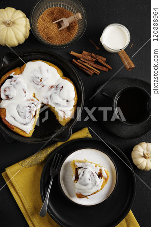 Cinnamon rolls with pumpkin in black pan and one lays on the plate on the black background, fall baking concept, to view Cinnamon rolls with pumpkin in black pan and one lays on the plate on the black background, fall baking concept, to view 120888964