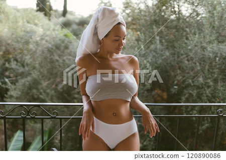 Young woman with a beautiful body wears sexy lingerie and poses on the balcony with a towel on her head 120890086