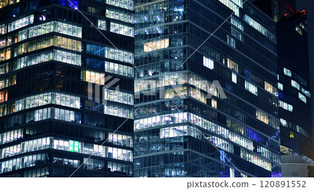 The glass facade of a modern skyscraper at night. Modern glass office in city. Big glowing windows in modern office building at night. In rows of windows light shines. 120891552