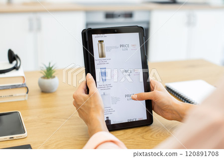 Caucasian woman browsing cosmetics on delivery website using tablet. She's seated in modern home setting, surrounded by notebooks and phone. 120891708