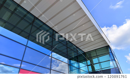 Fragment of a modern building made of steel and glass. Abstract modern commercial architecture fragment. Walls made of shiny glass and steel under blue sky. 120891761