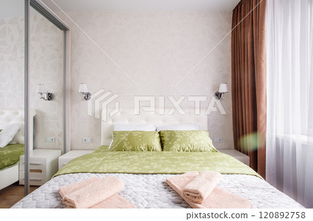 A well-appointed small modern bedroom with a cozy design, featuring a queen-sized bed, bedside tables. A large window with curtains allowing soft daylight. A well-appointed small modern bedroom with a cozy design, featuring a queen-sized bed, bedside tables. A large window with curtains allowing soft daylight. 120892758