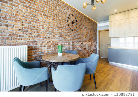 Elegant and comfortable kitchen interior with faux brick wall, round wooden table and armchairs. Elegant and comfortable kitchen interior with faux brick wall, round wooden table and armchairs. 120892781