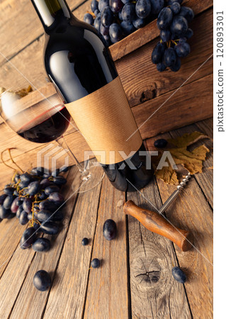 Bottle of red wine and blue grapes on a old wooden table. 120893301