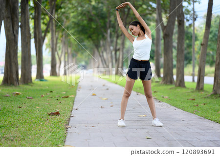 Portrait of young sportswoman enjoying a fitness session, stretching her arms in the park Portrait of young sportswoman enjoying a fitness session, stretching her arms in the park 120893691
