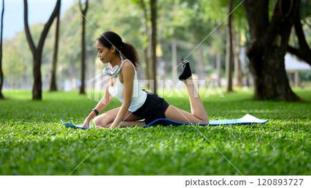Sporty young woman practicing yoga on green grass in a peaceful park 120893727