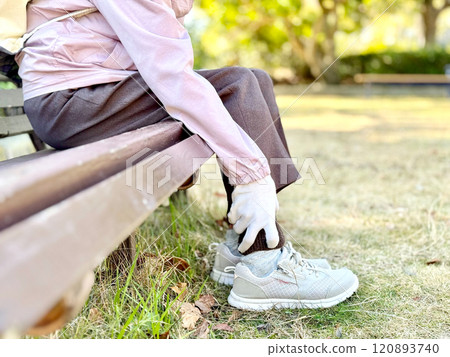 Elderly woman sitting on a bench and holding her ankle 120893740