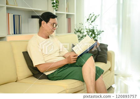 Senior asian man in casual clothes reading book on sofa at home 120893757