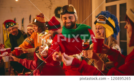 Joyful holiday celebration as friends in vibrant ski gear toast and laugh around rustic table lit with candles and sparkles, fireworks. Joyful holiday celebration as friends in vibrant ski gear toast and laugh around rustic table lit with candles and sparkles, fireworks. 120895265