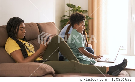 Woman using smartphone while brother and mother using laptop at home Woman using smartphone while brother and mother using laptop at home 120895655