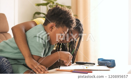 Little boy coloring in book with young sister on table at home Little boy coloring in book with young sister on table at home 120895657