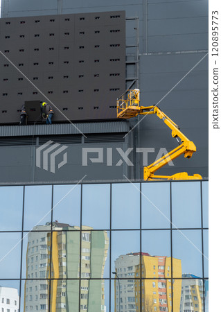 Two workers in hard hats mount elements of outdoor video advertising 120895773