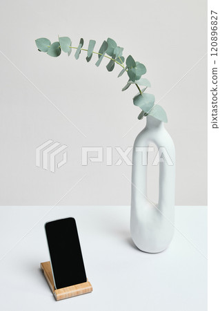 Phone, and vase with eucalyptus on neutral background. Balanced composition, offering negative space for promotional designs. Phone, and vase with eucalyptus on neutral background. Balanced composition, offering negative space for promotional designs. 120896827