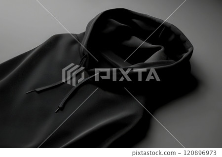 A black hoodie lies flat on a smooth, neutral background, highlighting its soft texture and minimalist design. The hood is slightly open, emphasizing the garments casual style. 120896973