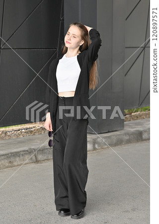 Woman walking in stylish outfit holding jacket on shoulder in urban environment on sunny day. 120897571
