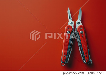 A multitool with red handles showcases its stainless steel blades and various tools. Placed on a solid red surface, it highlights versatility and practicality for outdoor activities or repairs. 120897729
