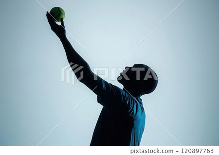 A player prepares to serve a tennis ball, captured in silhouette. The setting features a bright background that highlights the players focused expression and athletic form. 120897763