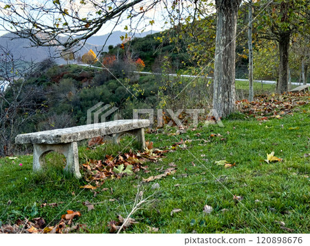 Rustic stone bench in a serene autumn landscape with trees and rolling hills 120898676