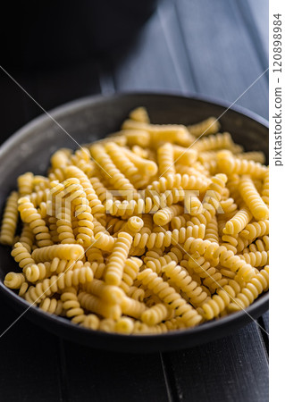 Uncooked italian pasta. Fusilli pasta in bowl on black table. 120898984