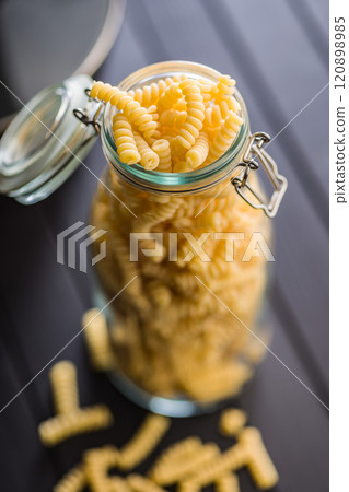 Uncooked italian pasta. Fusilli pasta in glass bottle on black table. Uncooked italian pasta. Fusilli pasta in glass bottle on black table. 120898985