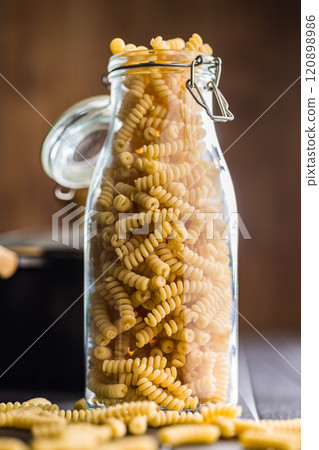 Uncooked italian pasta. Fusilli pasta in glass bottle on black table. Uncooked italian pasta. Fusilli pasta in glass bottle on black table. 120898986