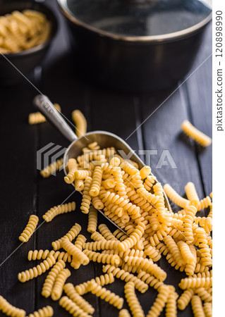 Uncooked italian pasta. Fusilli pasta in scoop on black table. 120898990