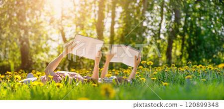 Mother and her child lying down on the green field with blooming flowers and reading books. 120899348