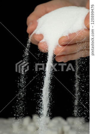 Hands pouring white crystalline refined sugar, black background 120899476